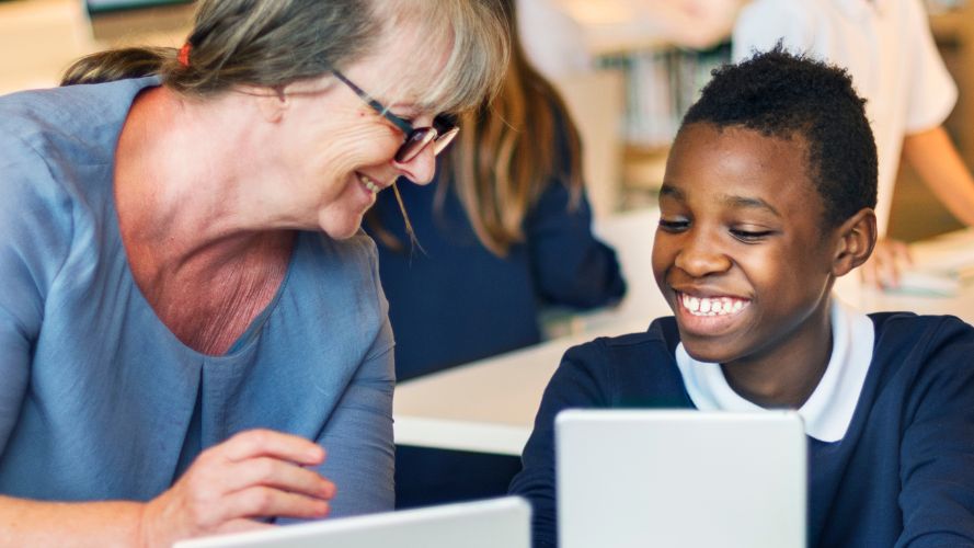 TA and young student smiling, sharing information using a tablet in class